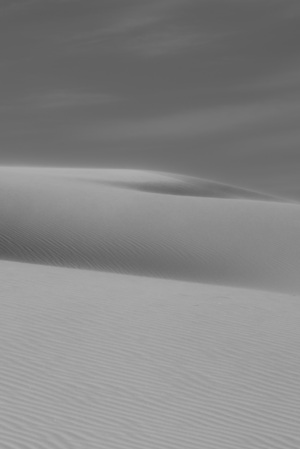 Black-and-white view of rippled gypsum dunes at White Sands National Park, with soft light accentuating the graceful curves and textures of the desert landscape.