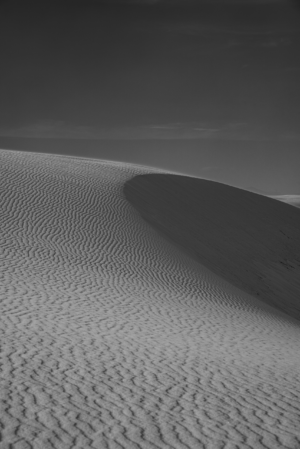 Black-and-white photograph of a sculpted gypsum dune at White Sands National Park, highlighting intricate ripple patterns and dramatic shadows across the desert landscape.