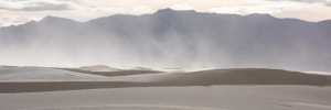 Windblown gypsum dunes at White Sands National Park with distant mountain peaks rising through drifting sand and soft desert light in New Mexico.
