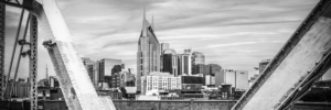 Black and white panoramic photograph of the Nashville Tennessee skyline framed by the John Seigenthaler Pedestrian Bridge