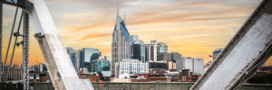 Panoramic Nashville Tennessee skyline at sunset framed by steel beams of the John Seigenthaler Pedestrian Bridge